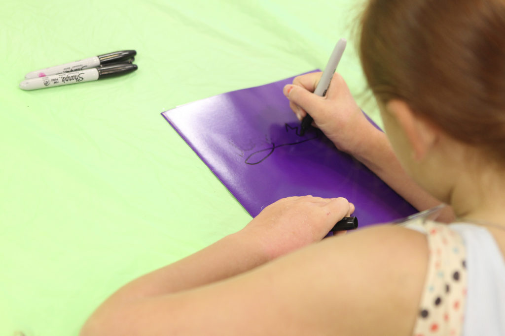 Young girl writes her name on a folder with a sharpie.