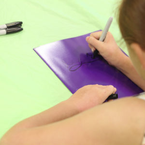 Young girl writes her name on a folder with a sharpie.