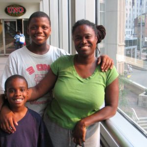 Mother and her two sons are standing infront of the window and they are smiling.