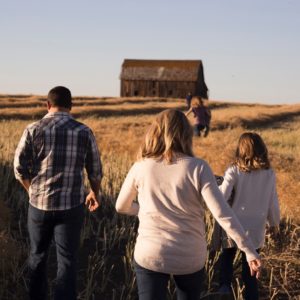 A young girl is walking towards her home through a corn field with her mother and father.